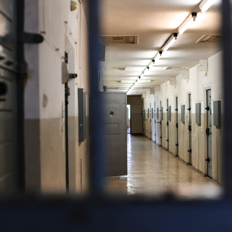 Long hallway of prison cells with bars in the foreground
